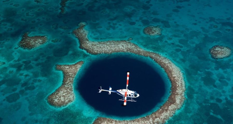 Ein Hubschrauber fliegt über das Great Blue Hole vor der Küste von  Belize – Image Source/Corbis ©