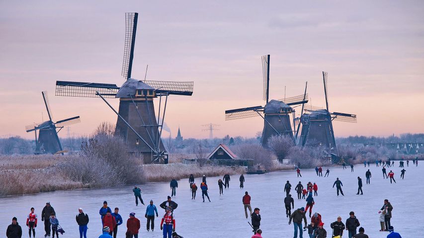 Schlittschuhläufer auf einem zugefrorenen Kanal in der Nähe der Windmühlen bei Kinderdijk, Niederlande